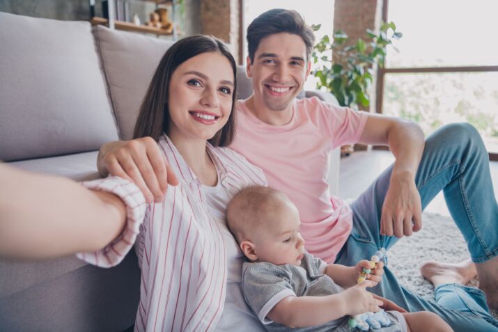 Un couple avec son bébé prend un selfie. Il sourit.